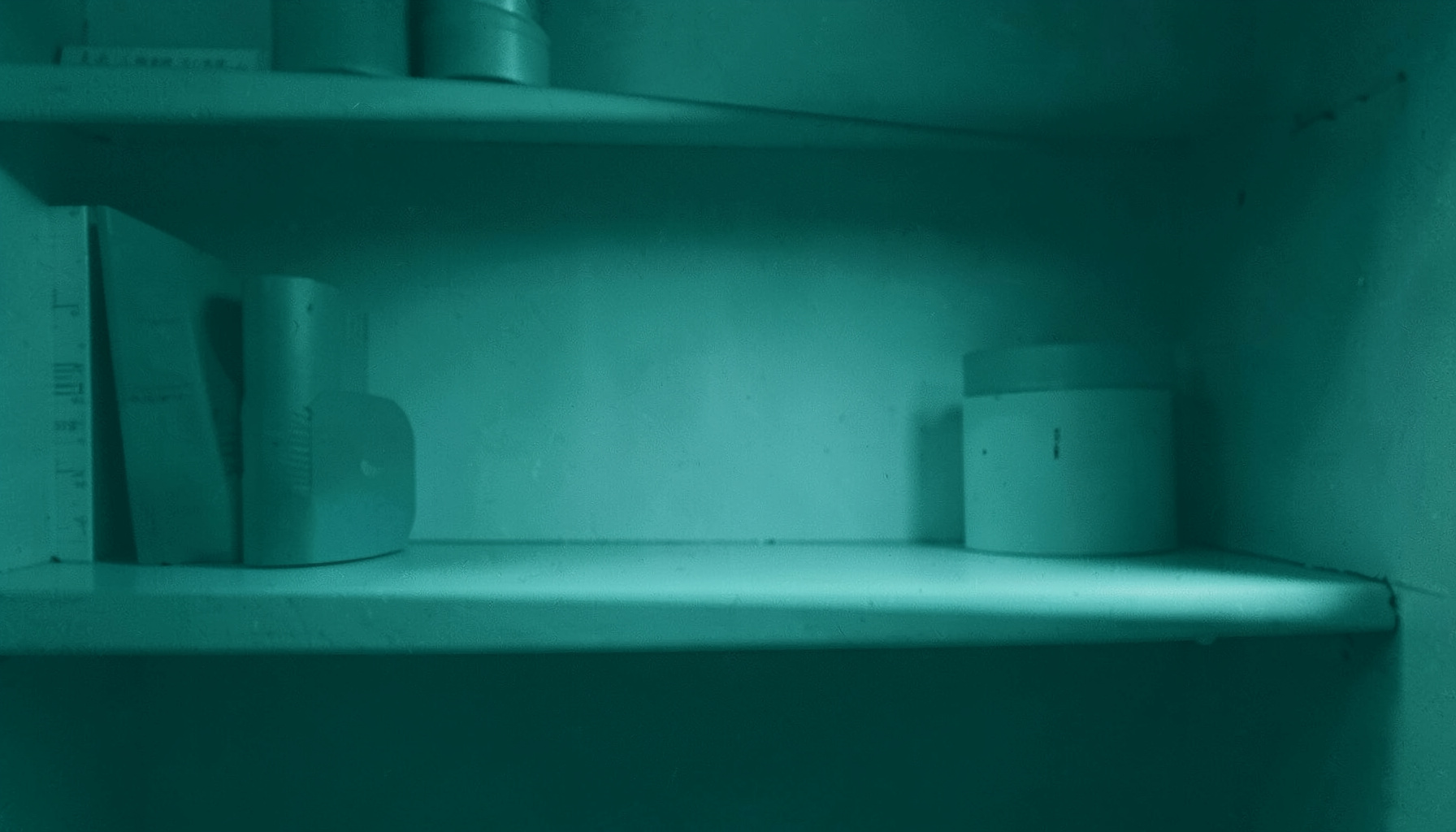 A duotone photograph in deep teal and pale cyan tones showing a softly lit shelf with a calm orderly atmosphere